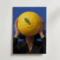 Citrus Surge Poster – kvinna håller jättelik citrusfrukt framför ansiktet mot koboltblå bakgrund